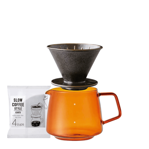 Kaffebryggare med orange glaskanna och metallfilter ovanpå samt paket med filterpåsar bredvid.