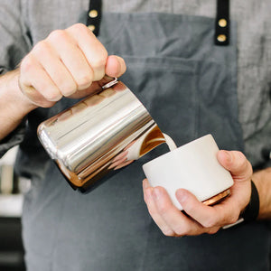 Barista verse du lait d'une verseuse polie en acier inoxydable, partie des accessoires Espresso et verseuse à lait, tout sur le café.