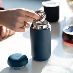 Main insérant un filtre dans une tasse à café réutilisable bleu mat, partie de Take away et EspressoGear, tout sur le café.
