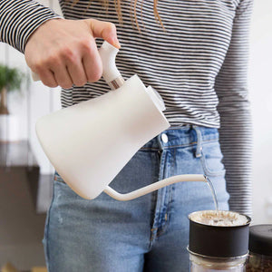 Main versant de l'eau d'une bouilloire blanche à bec étroit dans un filtre à café, partie d'EspressoGear, tout sur le café.