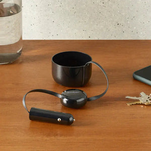 Chargeur de voiture pour tasse électrique Ember placé sur une table en bois avec adaptateur voiture et détails de réflexion.